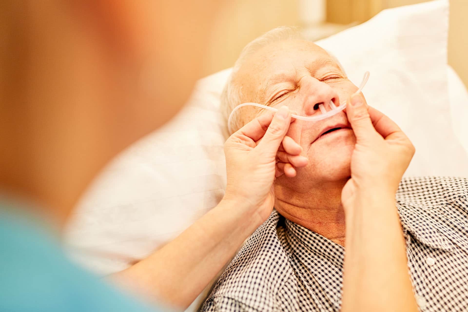 Pflegekraft kontrolliert die Sauerstoffbrille bei einem kranken Senior Mann
